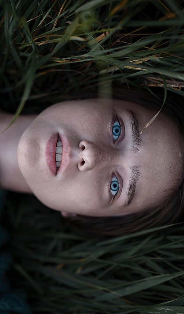 Голубоглазая девушка в свитере лежит на траве