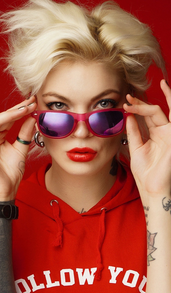 Яркая блондинка с татуировками на руках на красном фоне