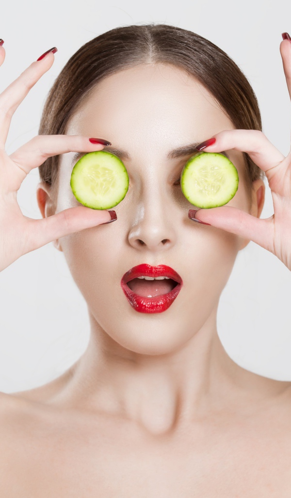 Яркая девушка с огурцами у глаз на сером фоне