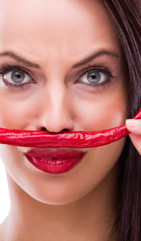 Брюнетка с красным перцем у лица на белом фоне