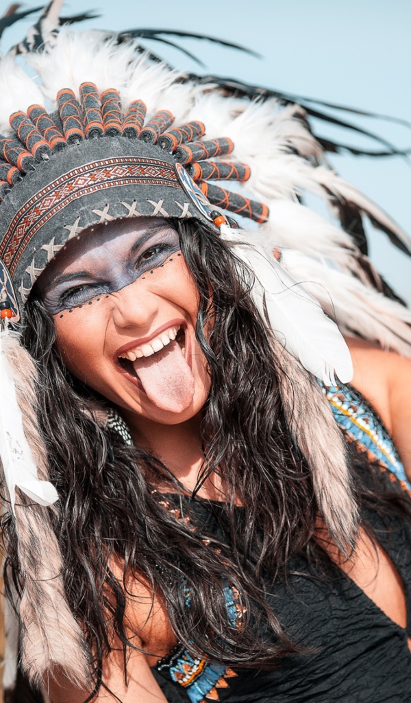 Веселая девушка с высунутым языком в костюме индейца
