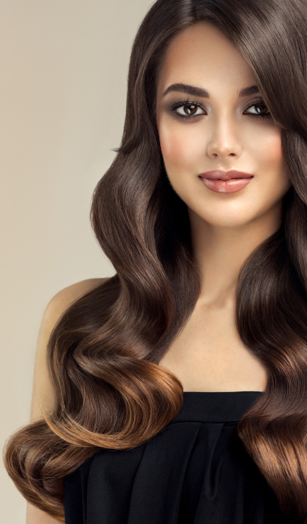 Милая кареглазая девушка с красивыми длинными волосами на сером фоне