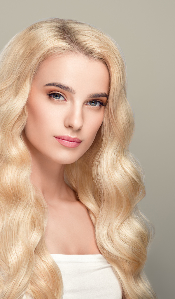 Милая длинноволосая блондинка на сером фоне