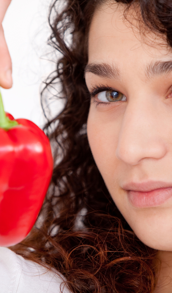 Лицо девушки с красным сладким перцем в руке крупным планом