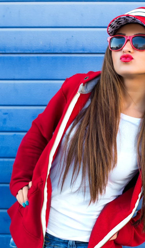 Девушка в бейсболке и солнечных очках у стены