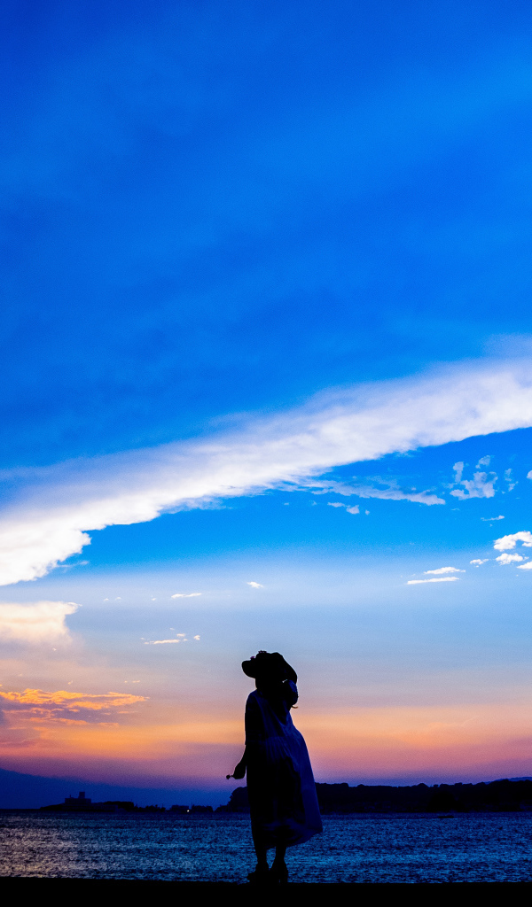 Девушка в шляпе смотрит на закат на берегу моря