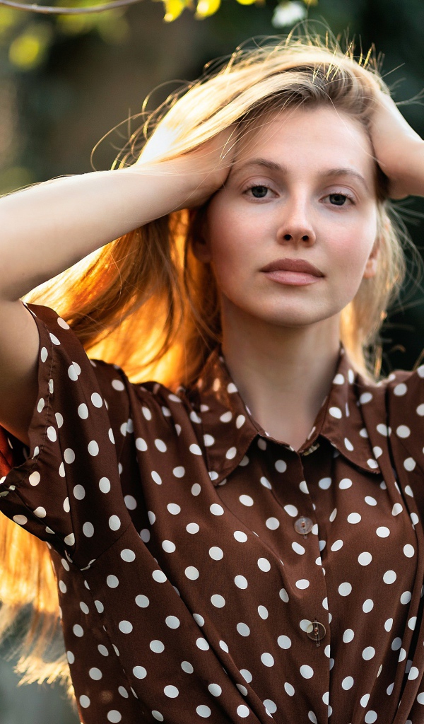Девушка в рубашке в горох с руками в волосах 
