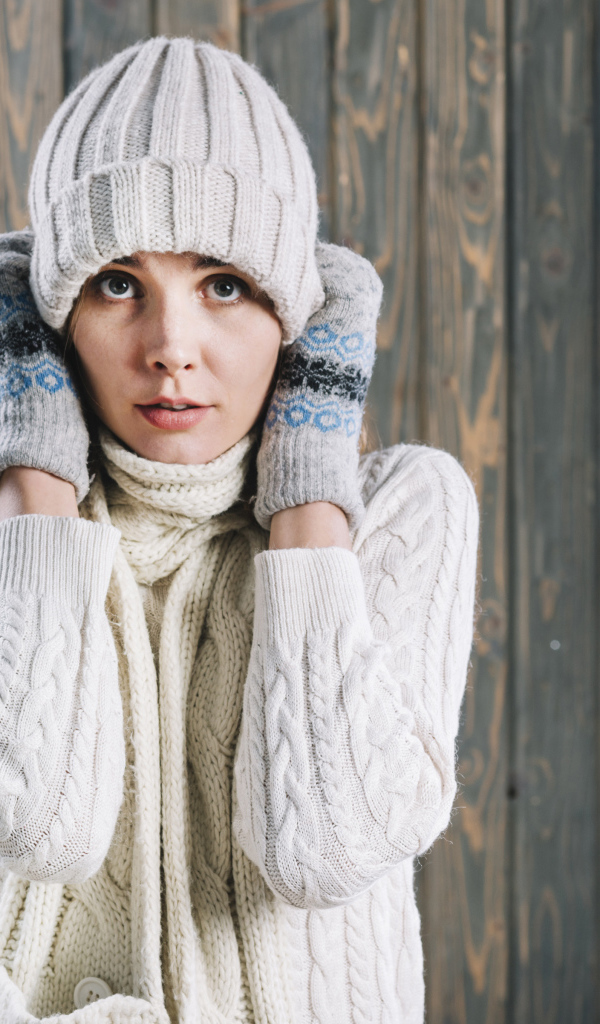 Девушка в варежках поправляет шапку на голове