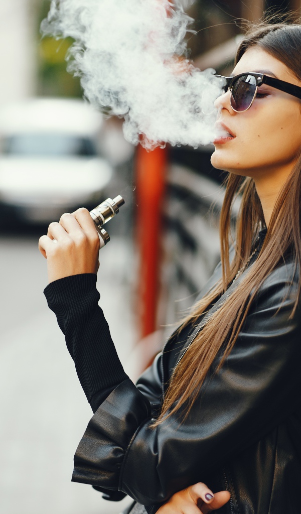 Девушка в солнечных очках пускает дым со рта