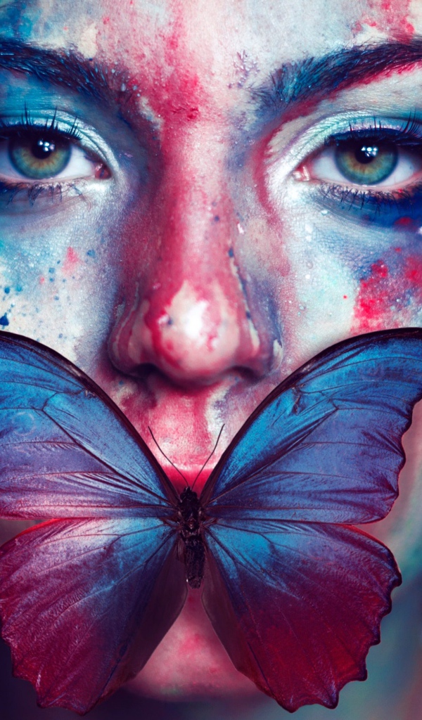 Лицо девушки в краске с бабочкой во рту