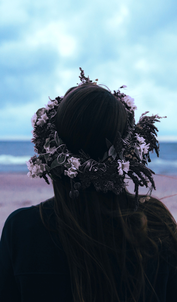 Девушка с венком на голове на фоне моря вид сзади