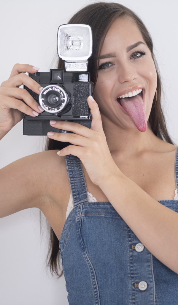 Девушка с высунутым языком с фотоаппаратом в руках