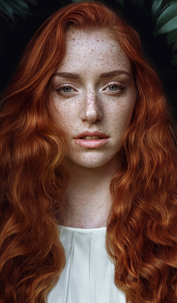 Рыжеволосая девушка с веснушками на лице на фоне кустов 