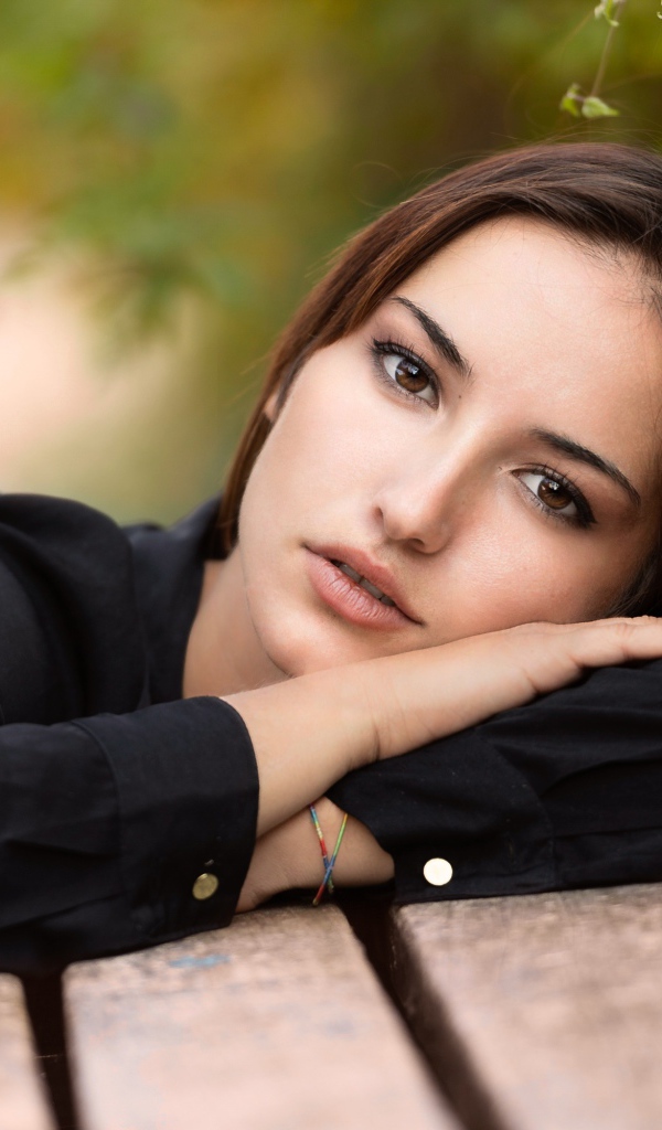 Грустная кареглазая девушка лежит на деревянной лавке