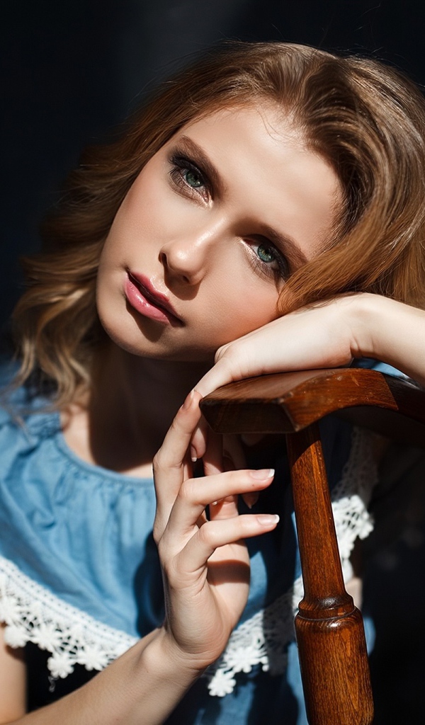 Грустная девушка сидит облокотившись об спинку кресла