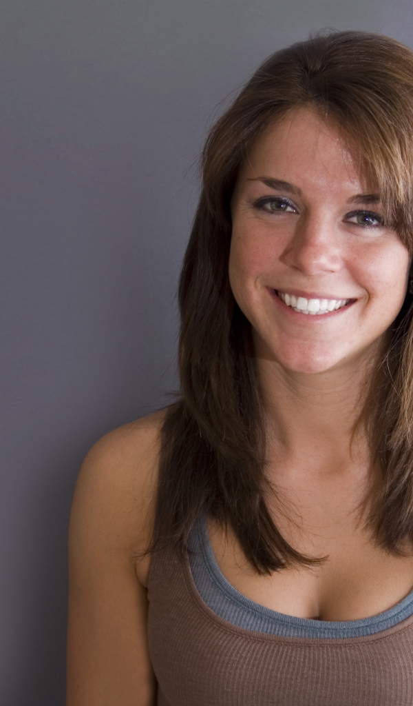 Улыбающаяся милая девушка у серой стены