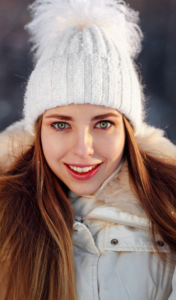Улыбающаяся девушка в теплой шапке и варежках зимой
