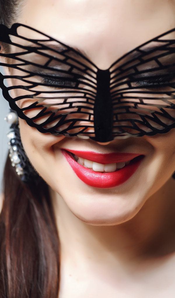 Улыбающаяся девушка в черной маске на сером фоне