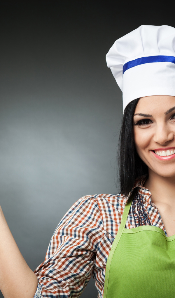 Улыбающаяся девушка в поварском колпаке на сером фоне