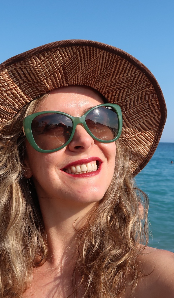 Улыбающаяся девушка в солнечных очках и шляпе на море