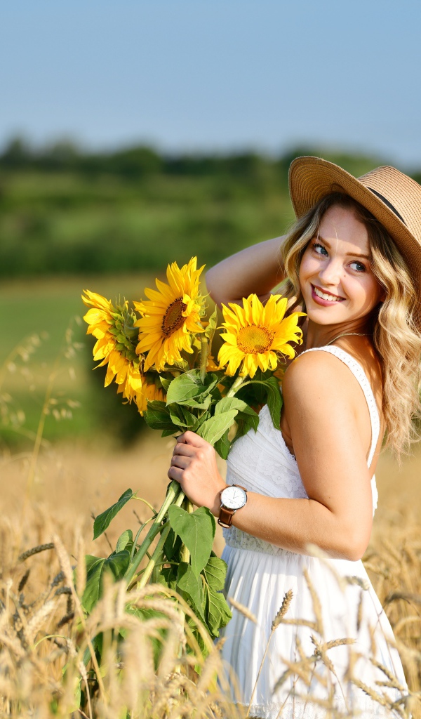 Улыбающаяся девушка на поле с пшеницей с букетом подсолнухов в руке
