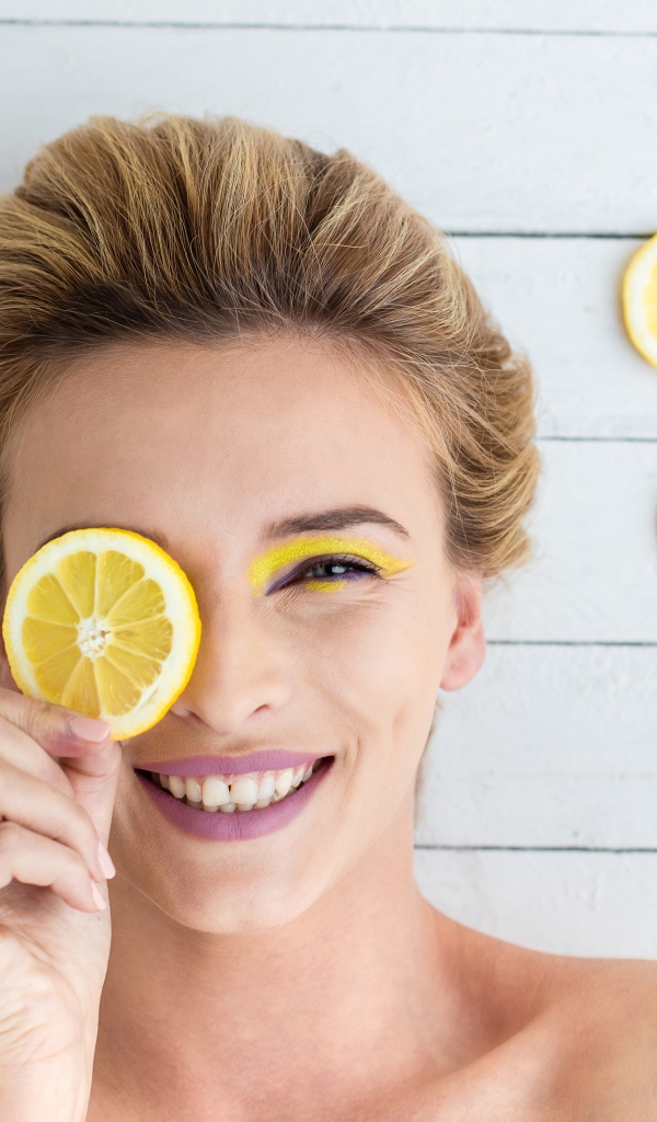 Улыбающаяся девушка приложила лимон к глазу