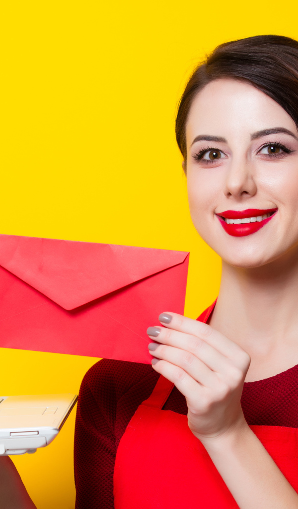 Улыбающаяся девушка с ноутбуком и конвертом в руках на желтом фоне