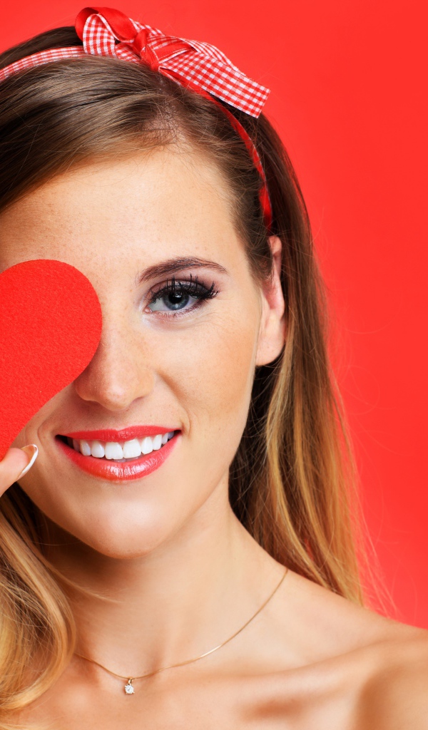 Улыбающаяся девушка с бумажным сердцем у лица на красном фоне
