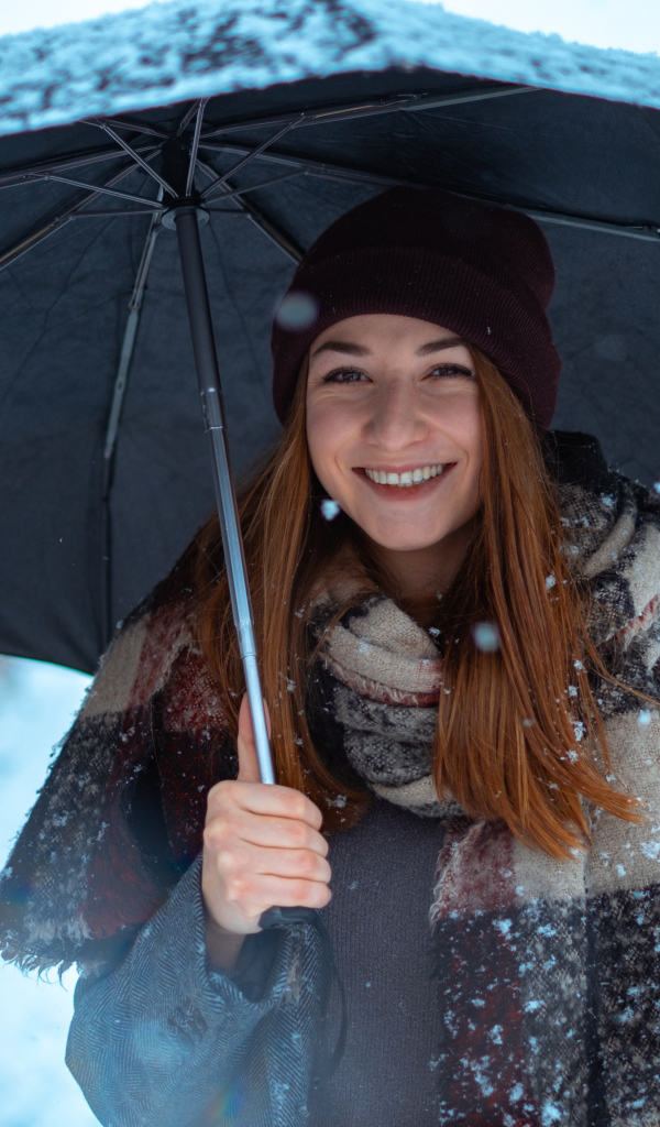 Улыбающаяся молодая девушка под зонтом зимой