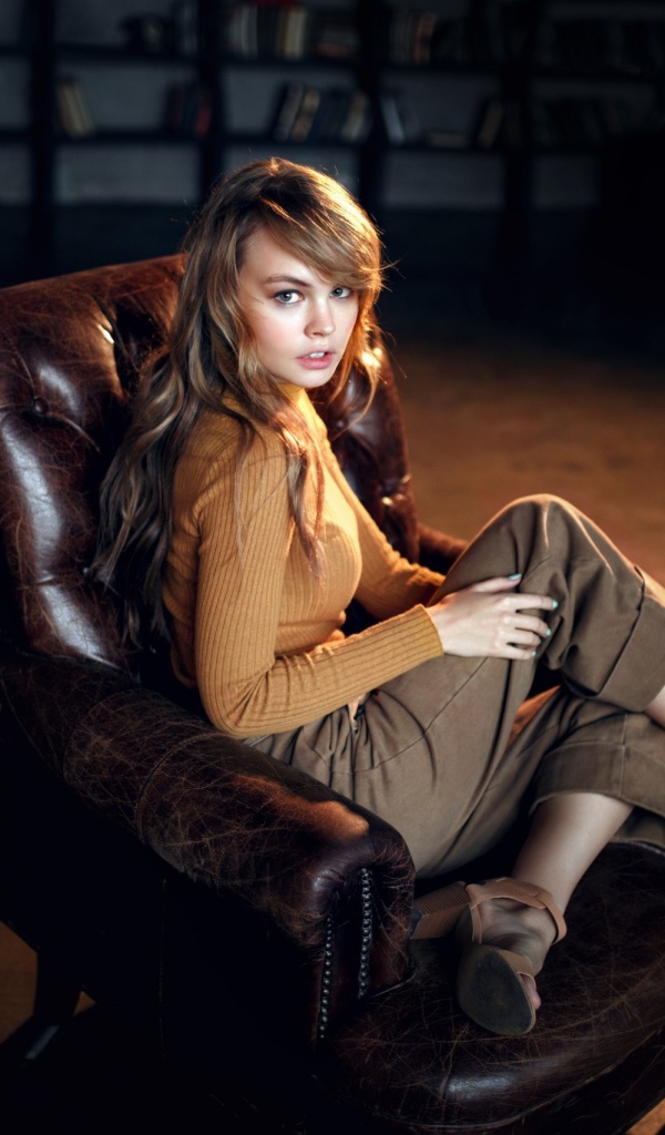 Нежная девушка модель сидит в кожаном кресле