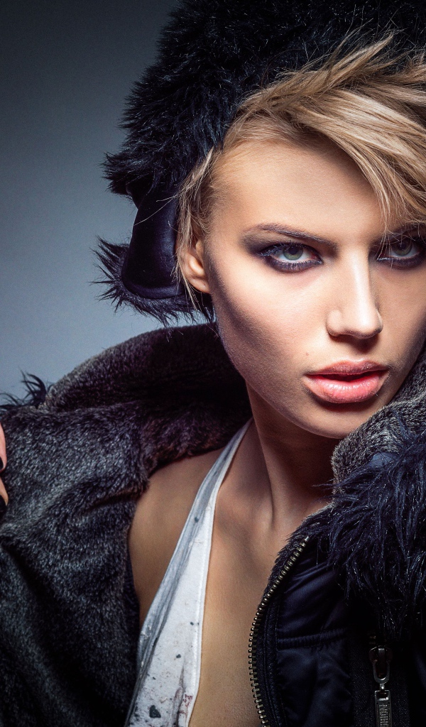 Девушка в теплой жилетке и шапке на сером фоне