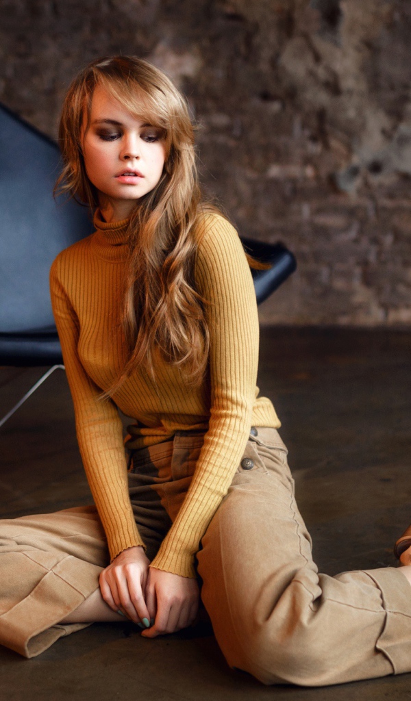 Девушка сидит на полу около черного кресла 