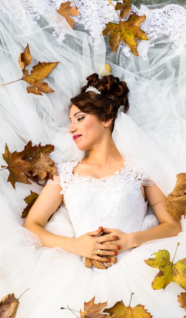 Девушка невеста в белом платье лежит с желтыми листьями
