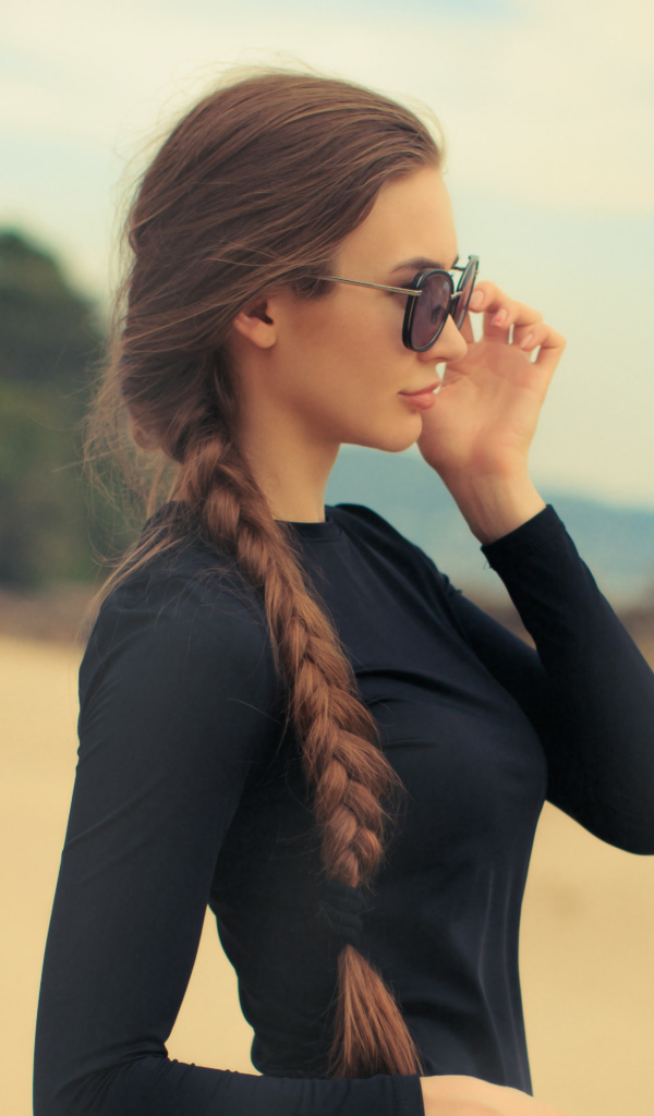 Девушка с косой в черных очках смотрит на воду