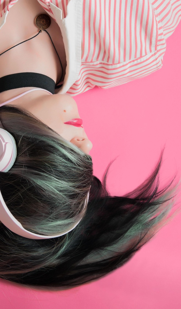 Девушка с наушниками на голове лежит на розовом фоне