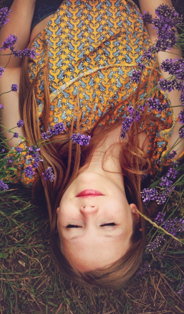 Девушка с закрытыми глазами лежит на земле с сиреневыми цветами
