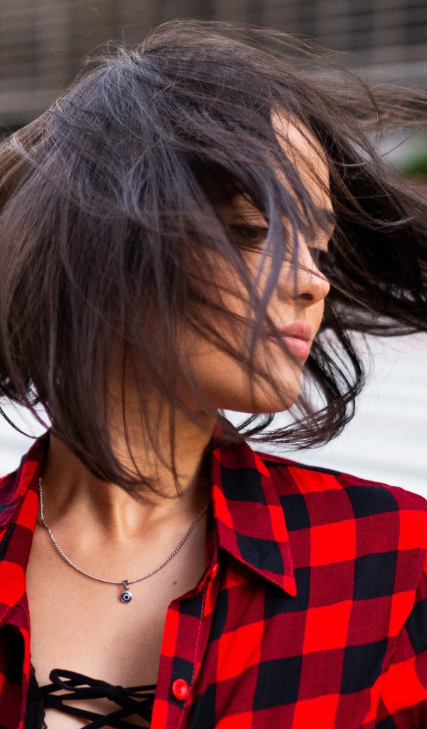 Ветер развивает волосы красивой шатенки в клетчатой рубашке