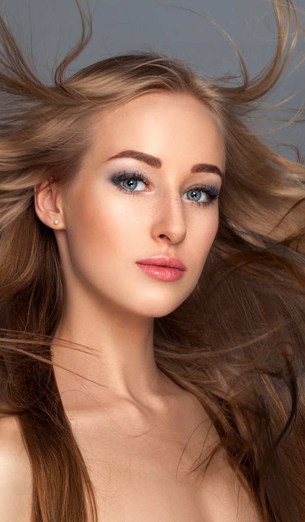 Ветер развивает волосы красивой девушке на сером фоне