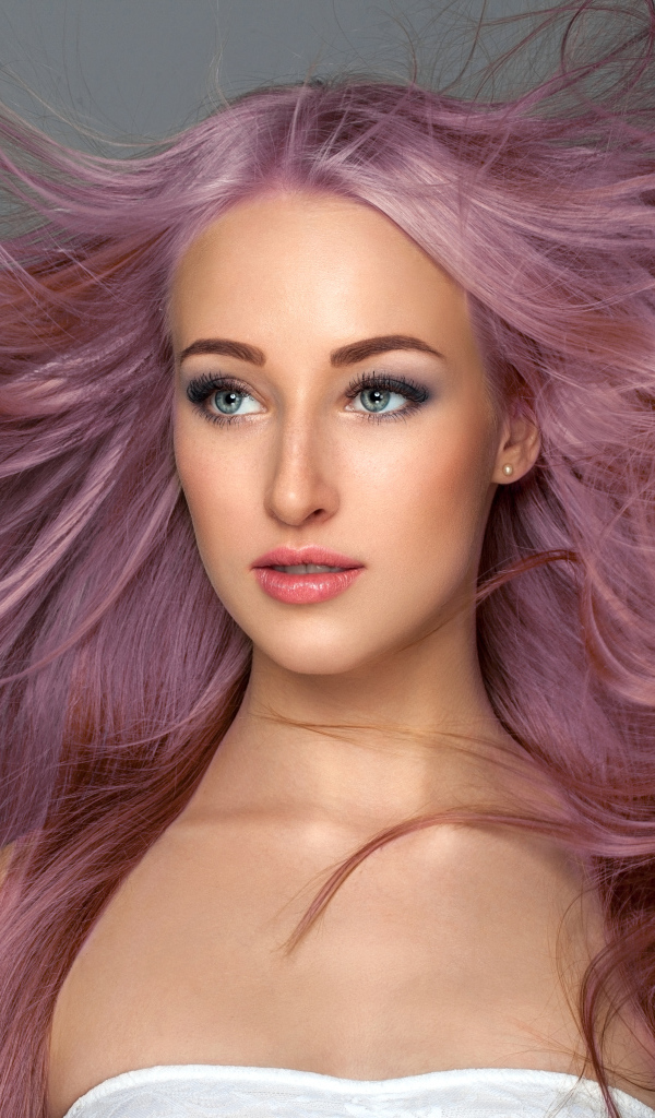 Ветер развивает розовые волосы девушки на сером фоне