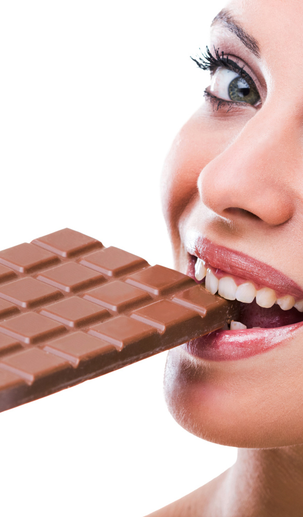 Молодая девушка кусает молочную шоколадку на белом фоне