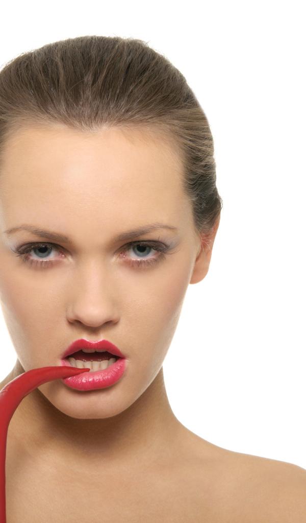 Молодая девушка кусает красный перец на белом фоне