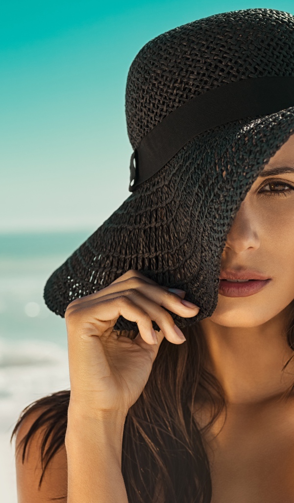 Молодая девушка в черной шляпе на берегу моря