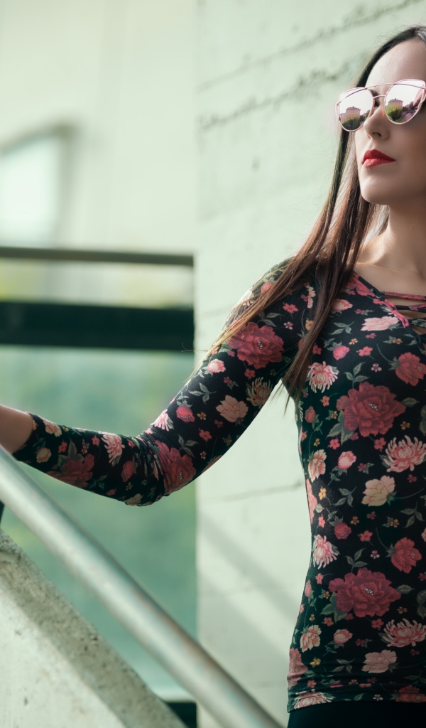 Молодая девушка в солнечных очках стоит на ступеньках