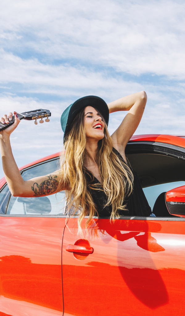 Молодая девушка с гитарой в красной машине летом