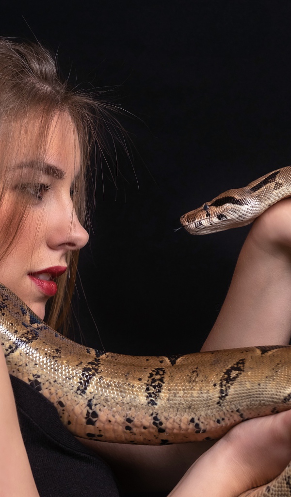 Молодая девушка со змеей в руках на черном фоне