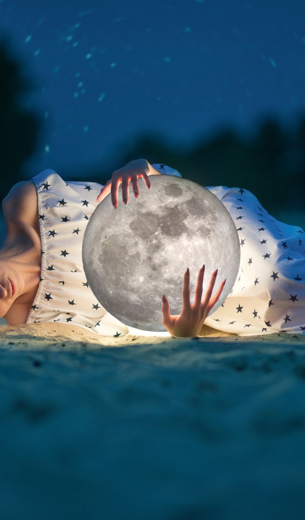 Молодая девушка с луной в руках лежит на песке