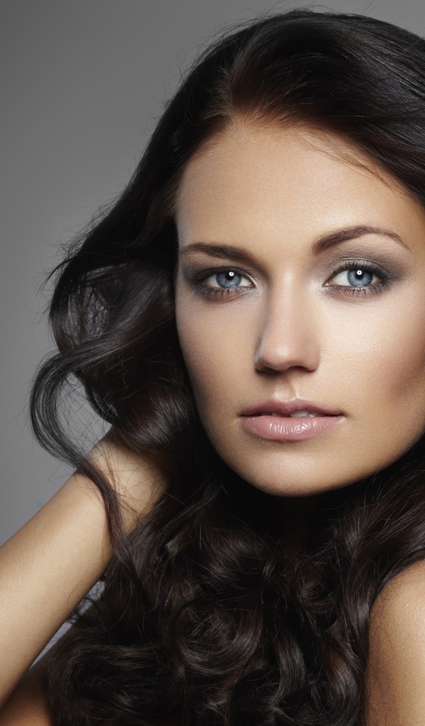 Молодая настоящая голубоглазая длинноволосая брюнетка на сером фоне