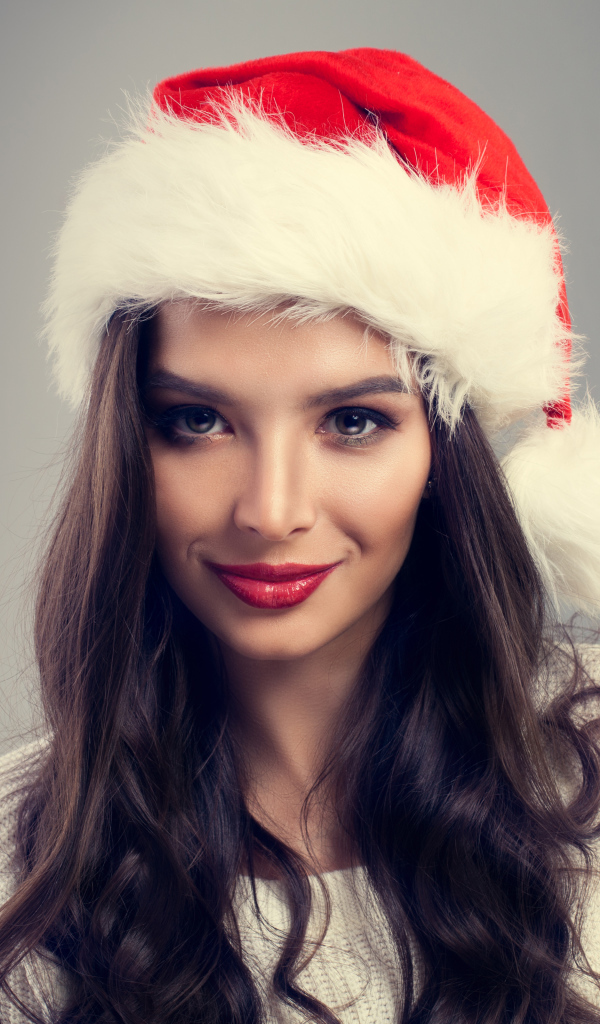 Красивая брюнетка в новогодней шапке на сером фоне