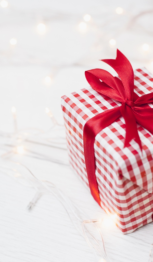 Подарок с красной лентой лежит на столе с гирляндой 