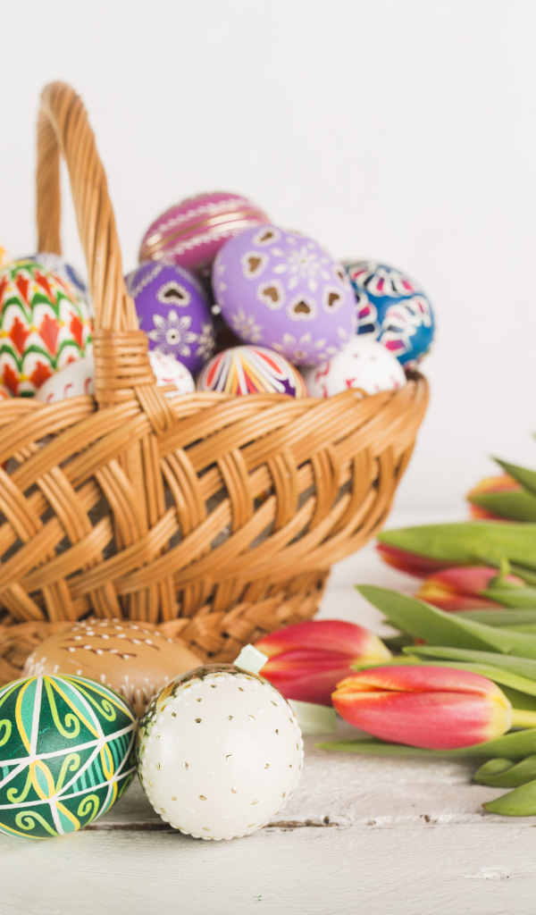 Корзина крашеных пасхальных яиц на белом фоне с букетом тюльпанов